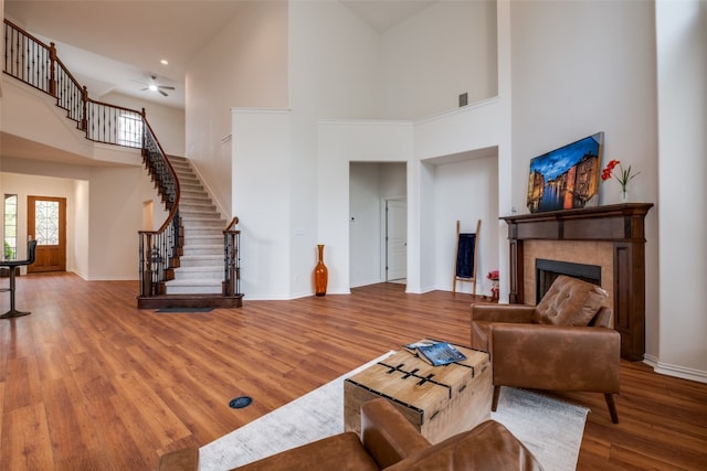 living room with a high ceiling, a tiled fireplace, and hardwood / wood-style floors