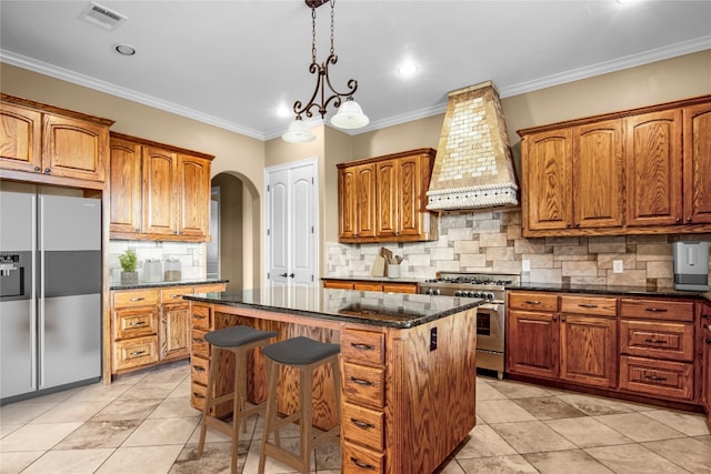 kitchen featuring appliances with stainless steel finishes, a kitchen island, backsplash, hanging light fixtures, and custom range hood