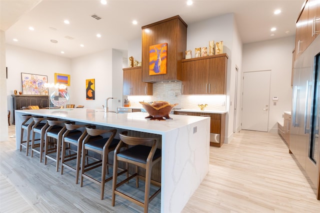 kitchen featuring sink, light hardwood / wood-style flooring, a breakfast bar area, backsplash, and a spacious island