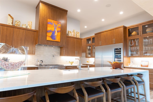 kitchen featuring sink, a kitchen bar, stove, stainless steel built in fridge, and light stone counters