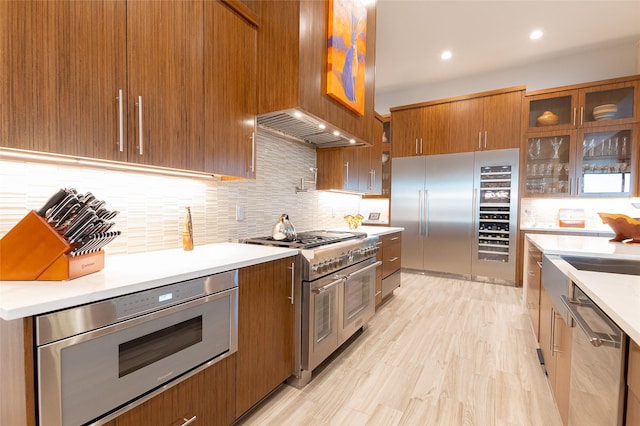 kitchen featuring tasteful backsplash, custom range hood, built in appliances, and light hardwood / wood-style floors