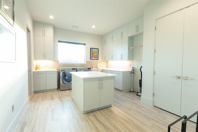 clothes washing area with cabinets, washer and dryer, and light wood-type flooring