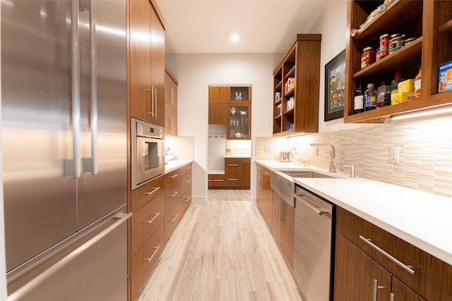 kitchen featuring sink, stainless steel appliances, tasteful backsplash, light stone counters, and light hardwood / wood-style floors