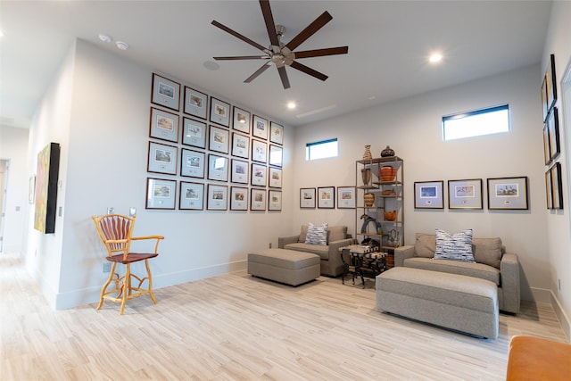 sitting room with a towering ceiling, ceiling fan, and light wood-type flooring