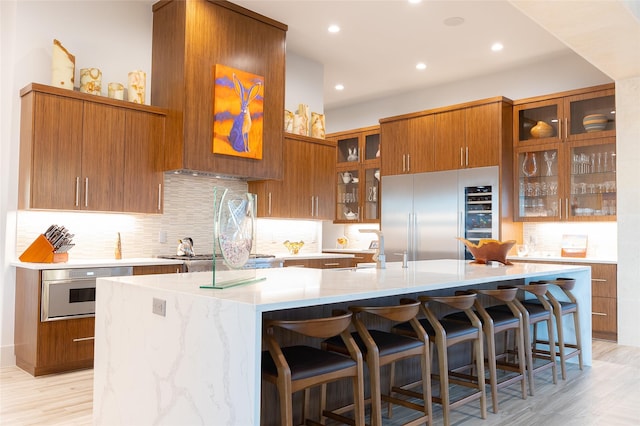 kitchen featuring light hardwood / wood-style flooring, appliances with stainless steel finishes, a kitchen breakfast bar, light stone counters, and a large island with sink