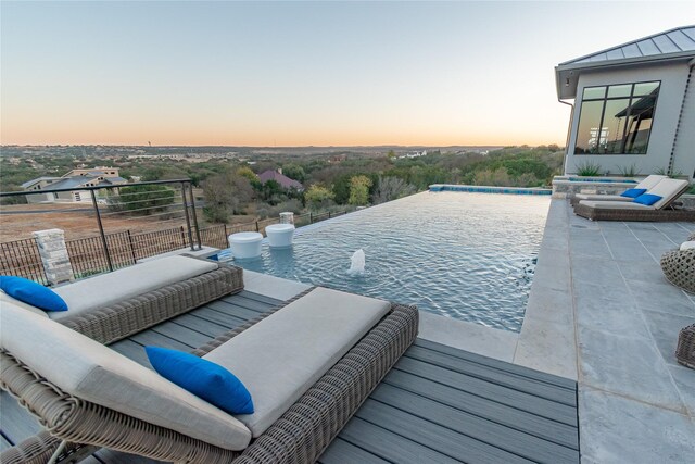 pool at dusk featuring pool water feature and a patio