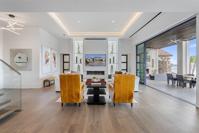 living room featuring a raised ceiling, ceiling fan with notable chandelier, and light hardwood / wood-style flooring