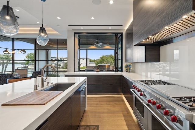 kitchen with light hardwood / wood-style floors, appliances with stainless steel finishes, hanging light fixtures, custom range hood, and sink