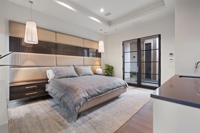 bedroom with a tray ceiling, hardwood / wood-style floors, access to outside, and sink