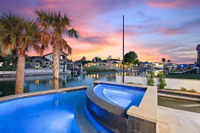 pool at dusk featuring a water view and an in ground hot tub