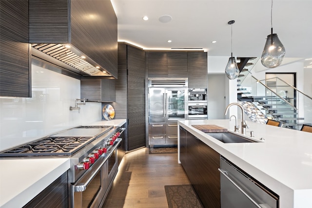 kitchen with pendant lighting, wall chimney range hood, dark hardwood / wood-style flooring, high quality appliances, and sink