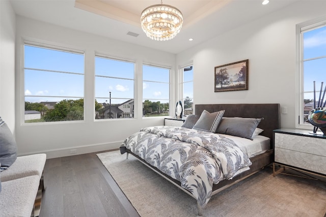 bedroom with a raised ceiling, multiple windows, a chandelier, and hardwood / wood-style flooring