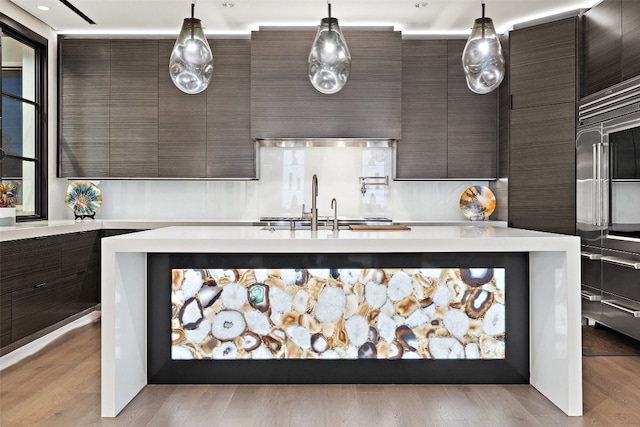 kitchen with a center island with sink, light hardwood / wood-style flooring, hanging light fixtures, and dark brown cabinetry