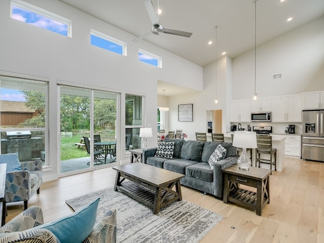 living room with a towering ceiling, ceiling fan, light hardwood / wood-style flooring, and plenty of natural light