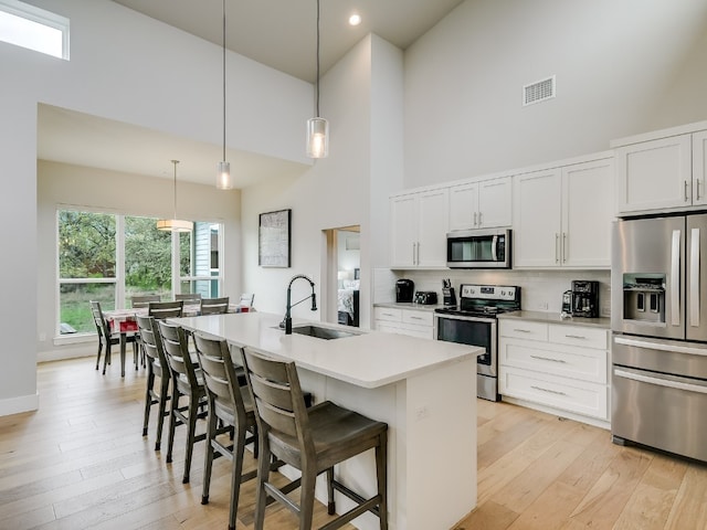 kitchen featuring stainless steel appliances, decorative light fixtures, tasteful backsplash, a towering ceiling, and white cabinets