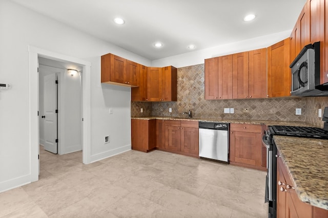 kitchen featuring brown cabinetry, a sink, light stone countertops, stainless steel appliances, and backsplash