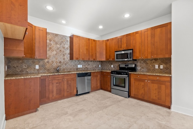 kitchen featuring tasteful backsplash, brown cabinetry, appliances with stainless steel finishes, light stone counters, and a sink