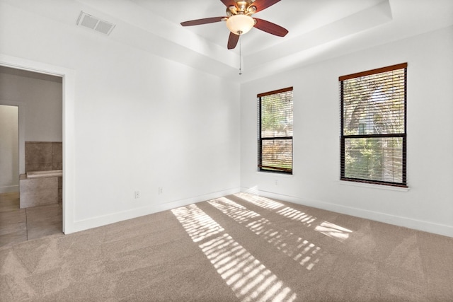 carpeted spare room featuring a ceiling fan, a tray ceiling, visible vents, and baseboards