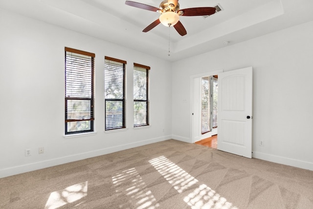 carpeted empty room with baseboards, a tray ceiling, and ceiling fan