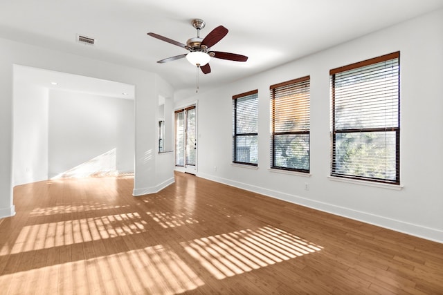 empty room featuring ceiling fan, wood finished floors, visible vents, and baseboards