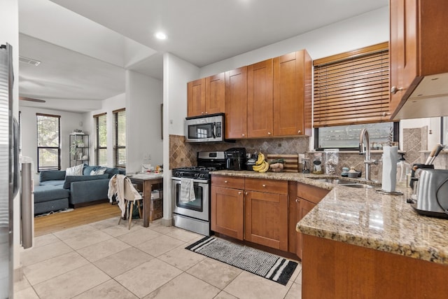 kitchen featuring light stone counters, light tile patterned floors, stainless steel appliances, decorative backsplash, and a sink