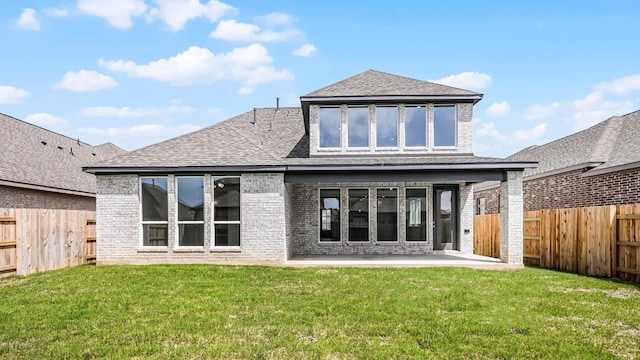 rear view of property with a shingled roof, a fenced backyard, a lawn, and brick siding