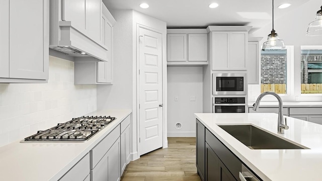 kitchen featuring hanging light fixtures, stainless steel appliances, light countertops, premium range hood, and a sink