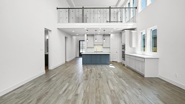 unfurnished living room with light wood-type flooring, a high ceiling, and baseboards