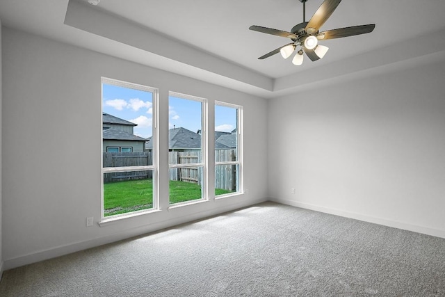 carpeted spare room featuring ceiling fan, a raised ceiling, and baseboards