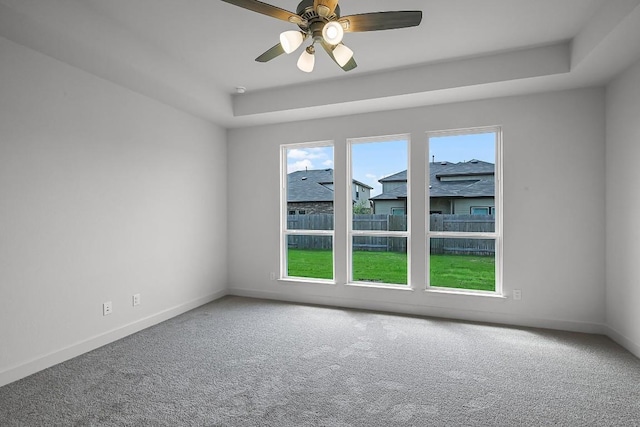 carpeted empty room featuring a tray ceiling, ceiling fan, and baseboards