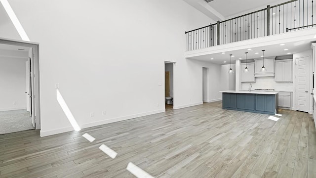 unfurnished living room with light wood-type flooring, a high ceiling, and baseboards