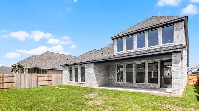 rear view of house with roof with shingles, a yard, brick siding, a patio area, and fence