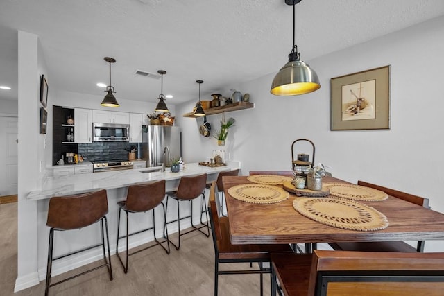 dining room featuring sink, a textured ceiling, and light hardwood / wood-style floors