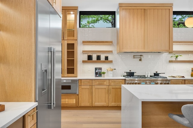 kitchen featuring light stone countertops, light hardwood / wood-style floors, appliances with stainless steel finishes, light brown cabinetry, and backsplash