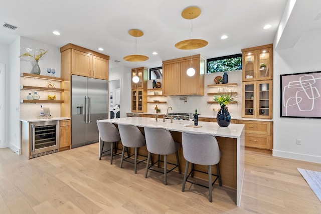 kitchen with hanging light fixtures, built in refrigerator, beverage cooler, backsplash, and light hardwood / wood-style floors