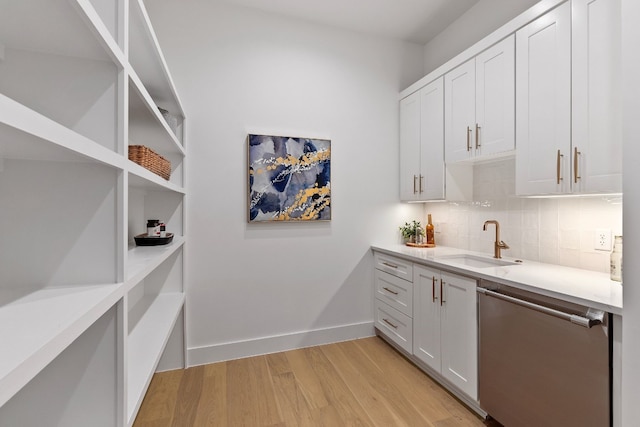 interior space featuring light wood-type flooring, stainless steel dishwasher, tasteful backsplash, sink, and white cabinetry