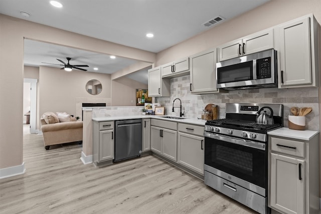 kitchen featuring sink, ceiling fan, backsplash, stainless steel appliances, and light wood-type flooring