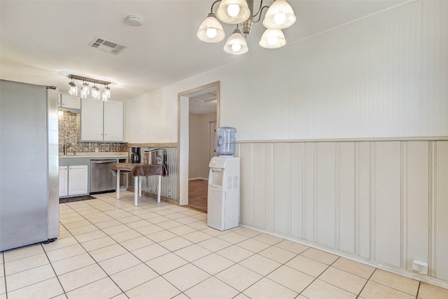 kitchen featuring tasteful backsplash, light tile floors, appliances with stainless steel finishes, an inviting chandelier, and white cabinetry