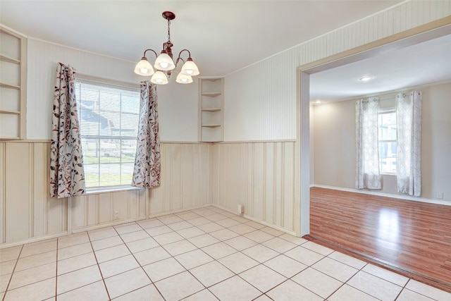 spare room featuring a chandelier, built in features, crown molding, and light tile floors