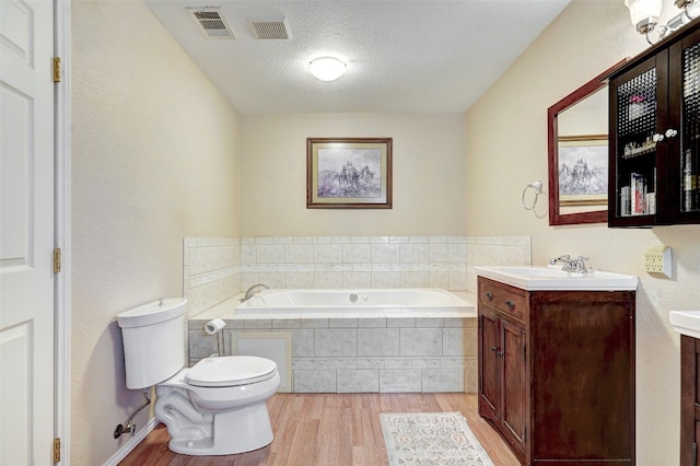 bathroom featuring wood-type flooring, a textured ceiling, a relaxing tiled bath, toilet, and vanity