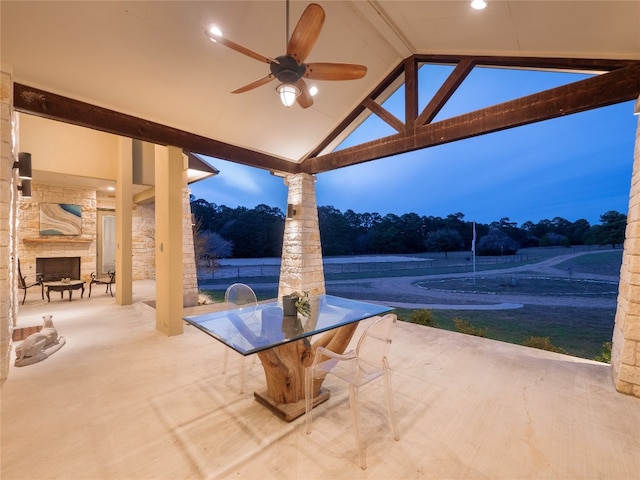 patio terrace at dusk with ceiling fan and an outdoor stone fireplace