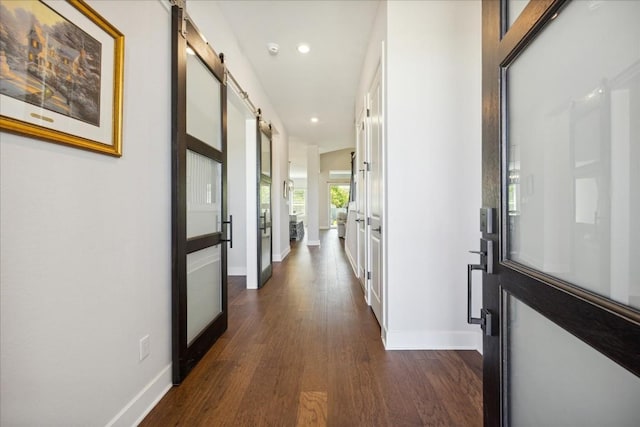 hallway featuring a barn door, dark wood finished floors, and baseboards