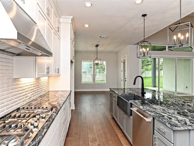 kitchen with appliances with stainless steel finishes, a sink, wall chimney range hood, and an inviting chandelier