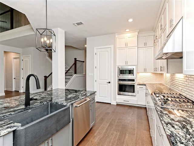 kitchen featuring dark wood-style flooring, stainless steel appliances, visible vents, a sink, and dark stone counters