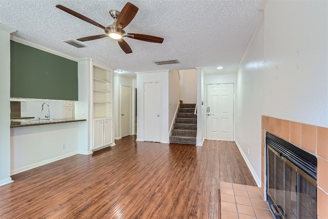 unfurnished living room featuring crown molding, a textured ceiling, a tile fireplace, wood-type flooring, and ceiling fan