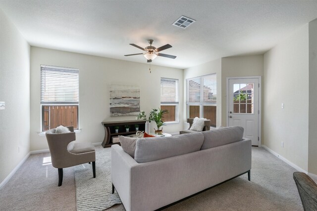 living room with a textured ceiling, ceiling fan, and light colored carpet