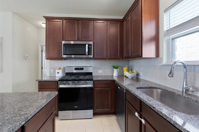 kitchen with light tile floors, appliances with stainless steel finishes, dark stone counters, and tasteful backsplash