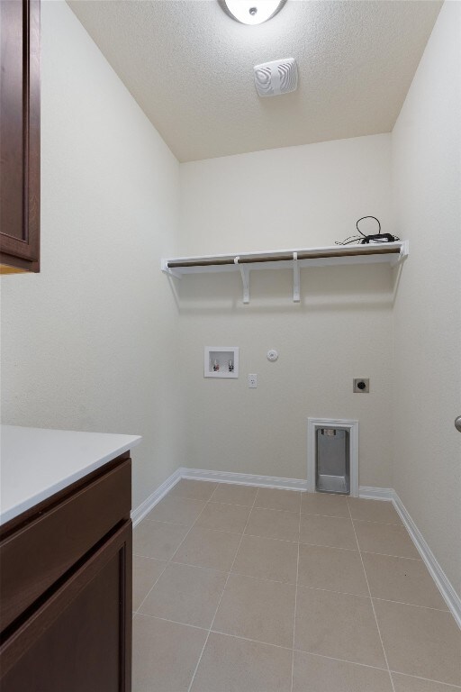 washroom featuring hookup for an electric dryer, hookup for a washing machine, light tile flooring, gas dryer hookup, and cabinets