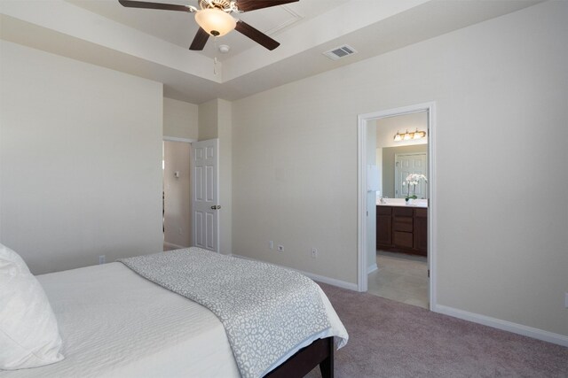 bedroom with ceiling fan, a raised ceiling, light carpet, and ensuite bathroom