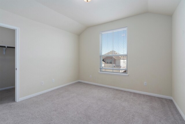 unfurnished bedroom with a closet, light carpet, a walk in closet, and vaulted ceiling